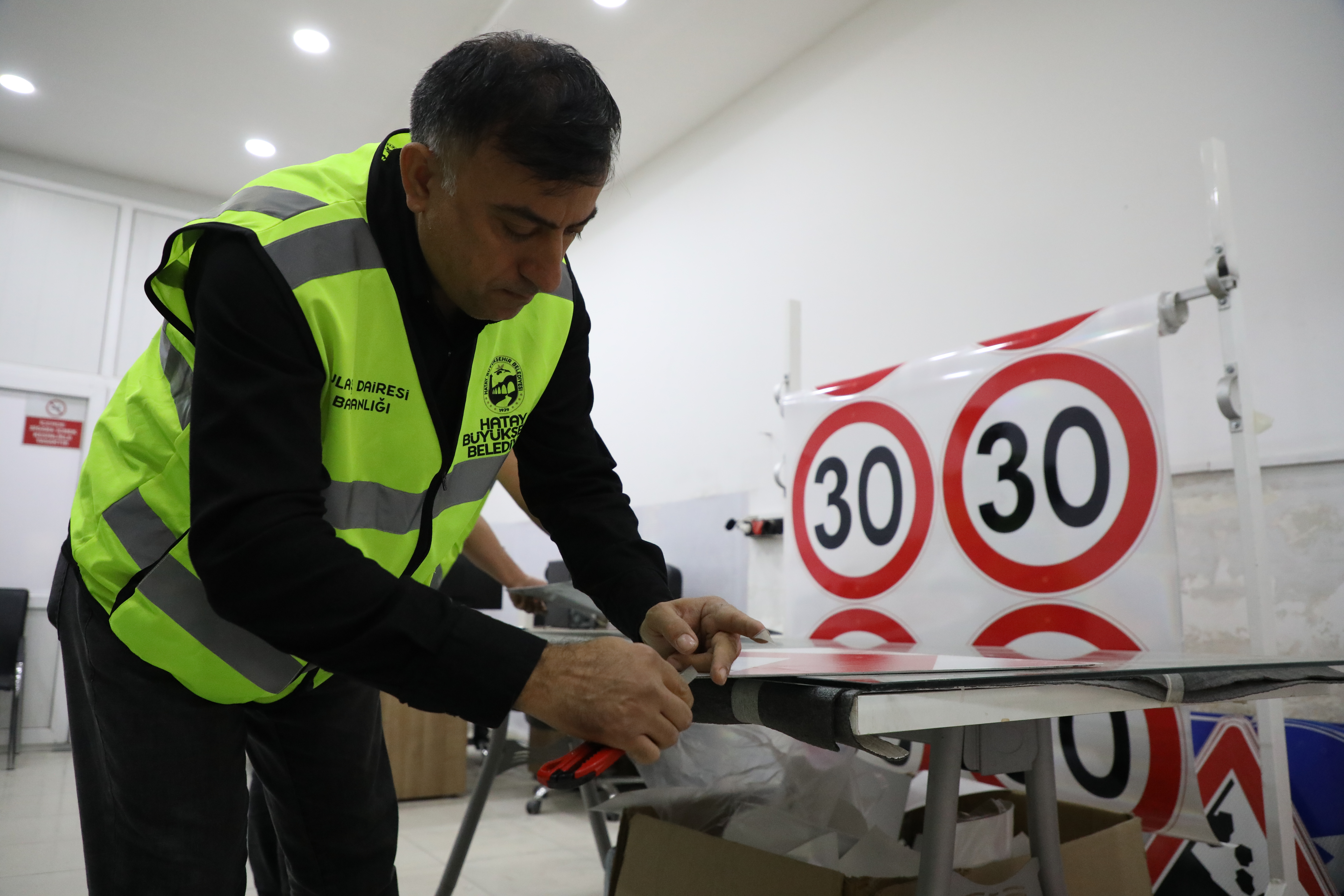 Hatay Büyükşehir Belediyesi, deprem sonrası şehirdeki adres belirsizliklerini gidermek ve güvenli ulaşımı sağlamak için fosforlu levhalar yerleştiriyor. Yeni levhalar gece görünürlüğü artırıyor.